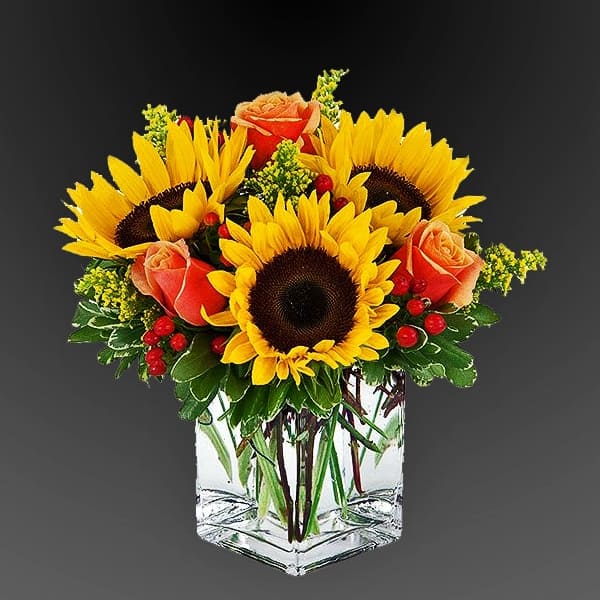 Sunflowers and orange roses arranged in a clear square vase