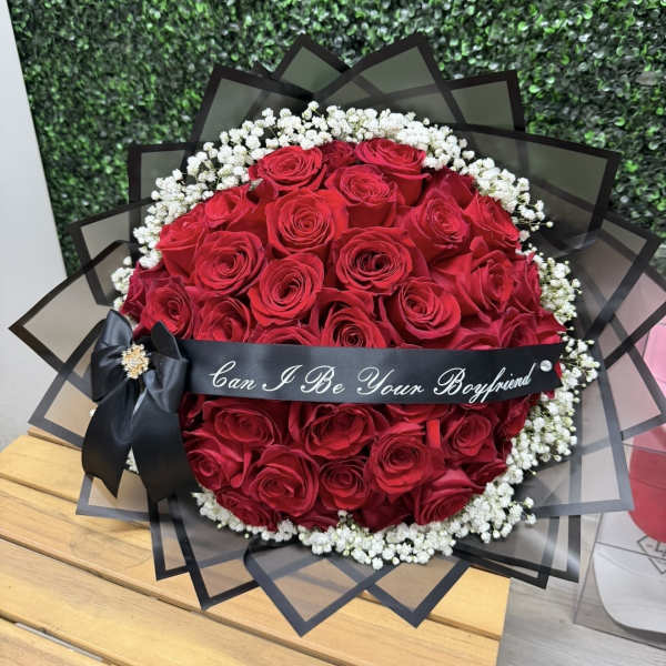 Round bouquet of red roses with white baby's breath and a black ribbon.