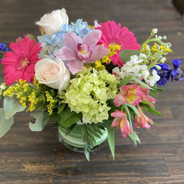 Mixed bouquet in a striped vase with pink daisies, roses, hydrangea, and orchids