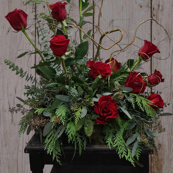 Red roses arranged in a low black container with curly branches