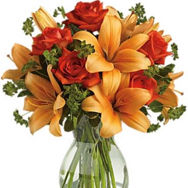 Bouquet of orange lilies and red roses in a clear glass vase