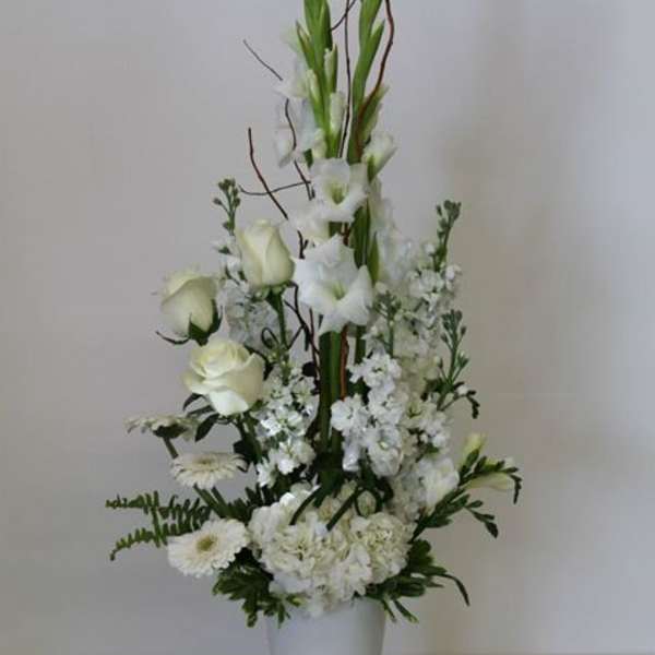 Tall white floral arrangement with roses and mixed blooms in a white vase