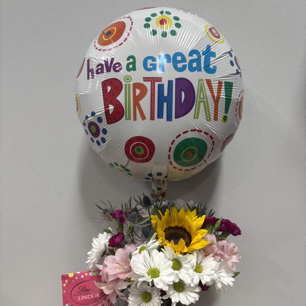 Birthday balloon above a mixed flower bouquet with chocolates in a vase