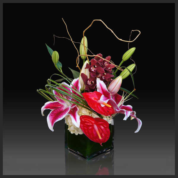 Tropical floral arrangement with lilies and orchids in a square vase