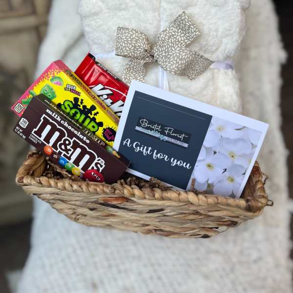 Gift basket with a white plush blanket, candy boxes, and a florist card
