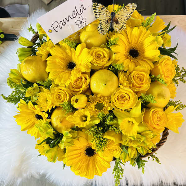 Round yellow flower basket with gerbera daisies, roses, lemons, and a name card topped with a butterfly.