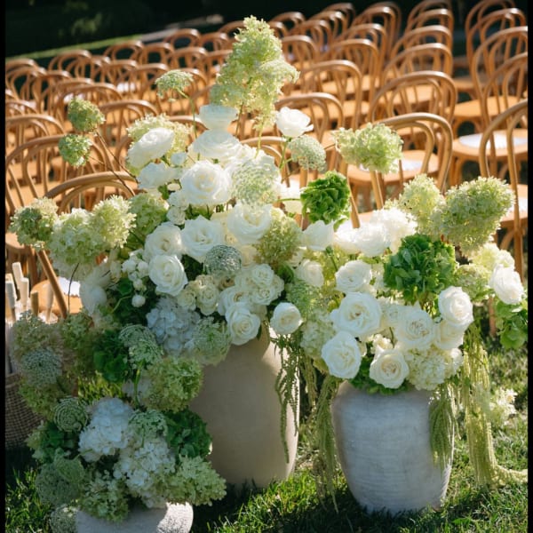 White rose and hydrangea arrangements in stone vases at outdoor wedding seating