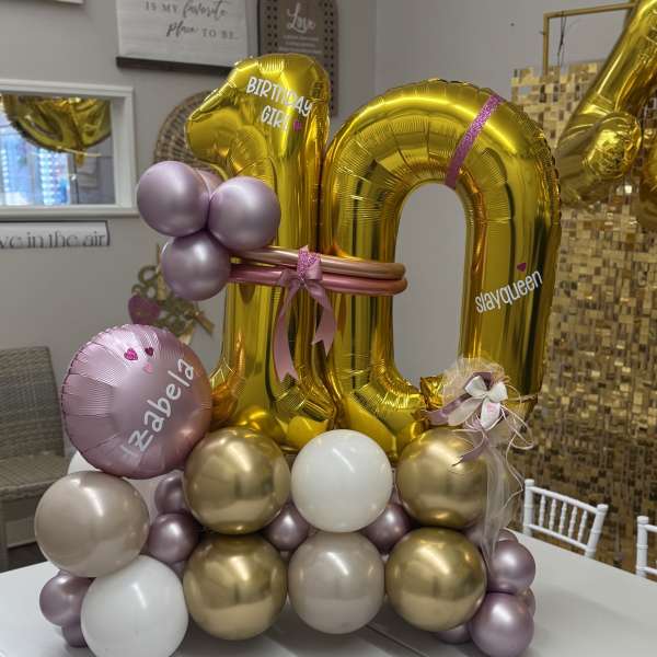 Gold birthday balloon display with pink and lavender accents on a table