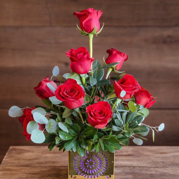 Red roses arranged in a gold square vase with eucalyptus accents