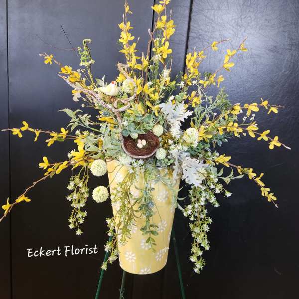 Yellow floral arrangement in a decorative vase with a small bird nest accent