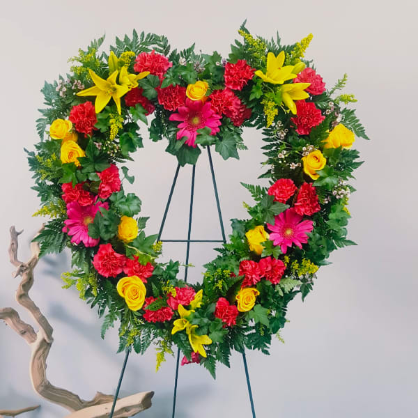 Heart-shaped floral wreath on a stand with red, yellow, and pink flowers