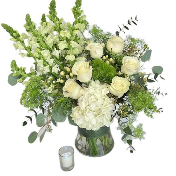 White roses and hydrangea in a glass vase with a small candle