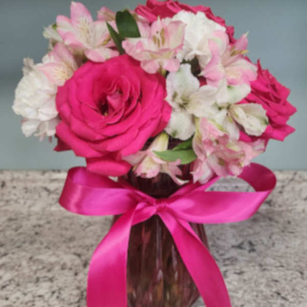 Pink and white flowers arranged in a glass vase with a pink ribbon