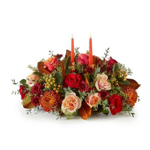 Low floral centerpiece with red and peach roses and two orange taper candles