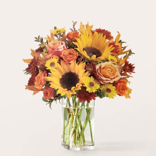Bouquet of sunflowers, roses, and mums in a clear glass vase