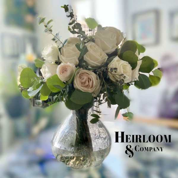 White and blush roses in a clear glass vase with greenery