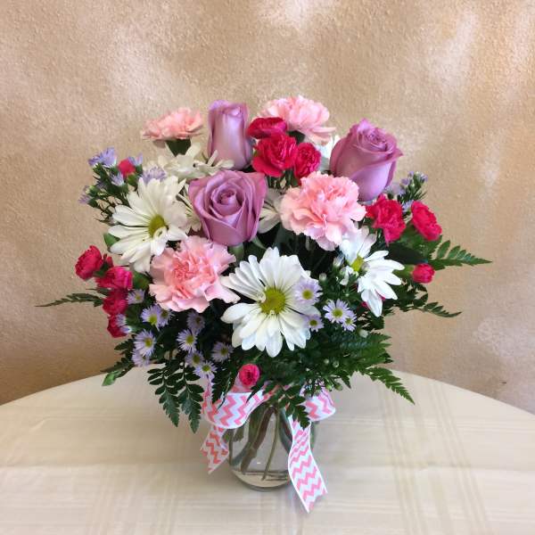 Mixed bouquet of pink and purple roses, carnations, and daisies in a glass vase