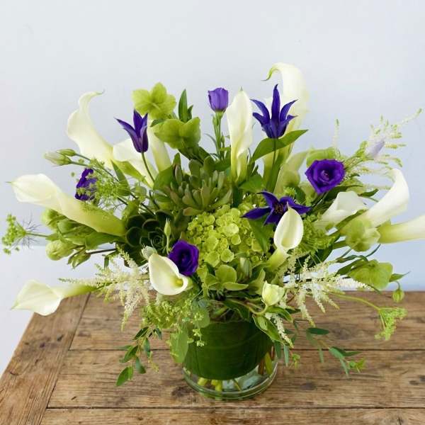 White calla lilies and purple flowers in a glass vase