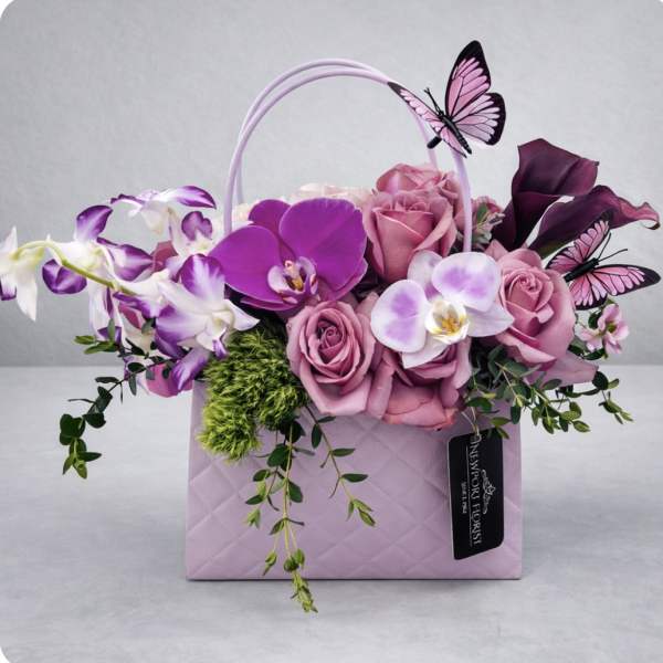 Pink and purple flowers arranged in a lavender gift bag with butterfly decorations