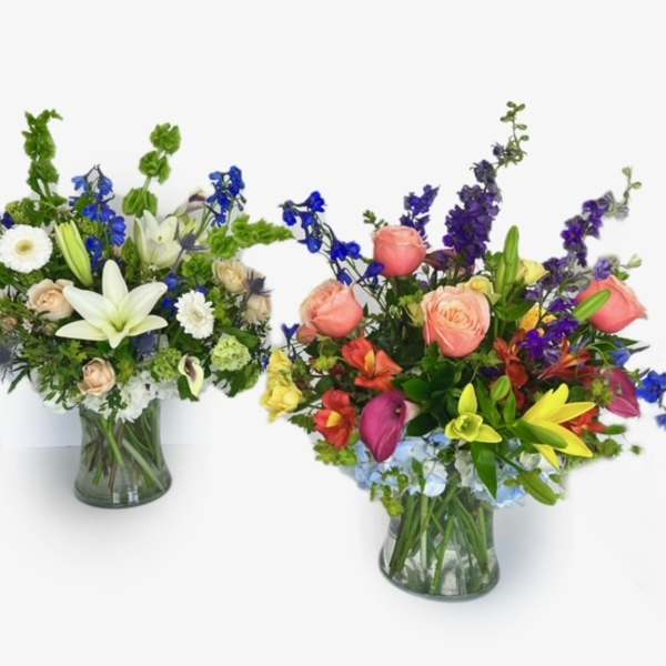 Two mixed flower arrangements in glass vases, one white and blue and one pink, yellow, and purple.
