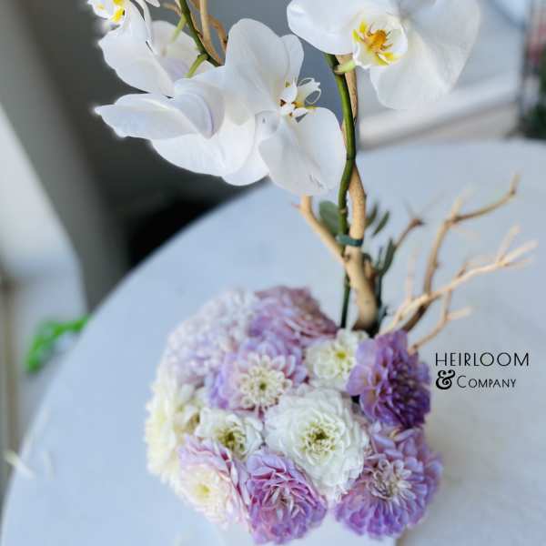 White orchids above a pastel pink and lavender floral arrangement in a white vase