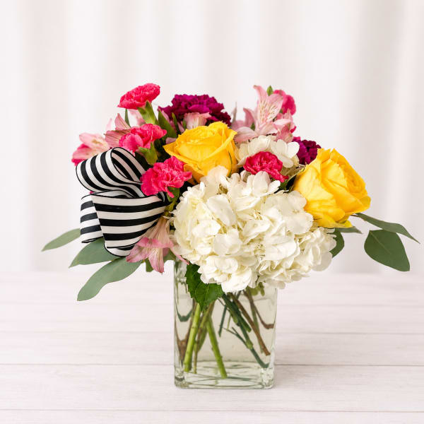 Bouquet of yellow roses, white hydrangea, and pink flowers in a glass vase