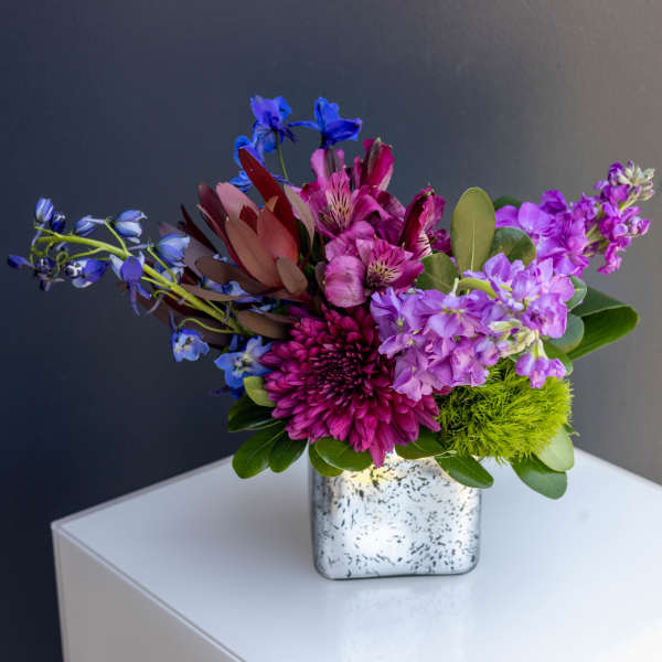 Colorful bouquet in a speckled square vase with purple and blue flowers
