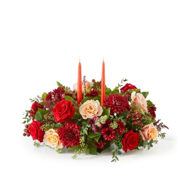 Low floral centerpiece with red and peach roses and two orange taper candles