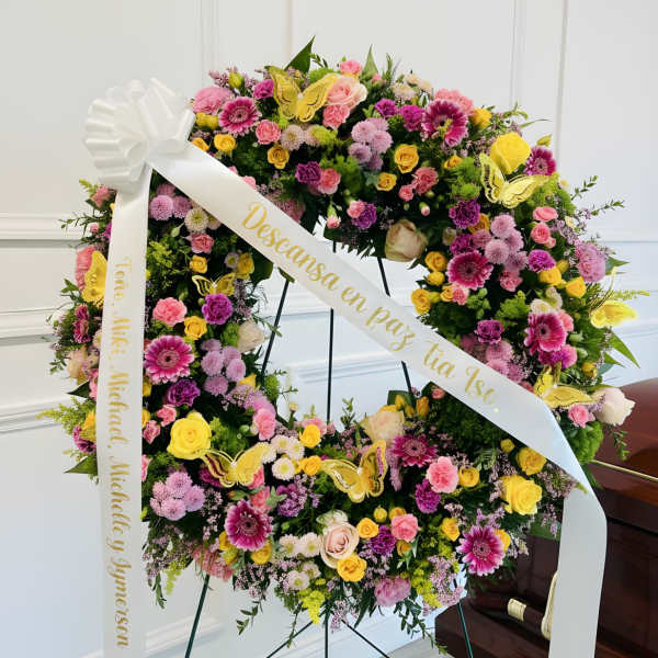 Large floral wreath with pink, yellow, and purple blooms on a stand with white ribbons
