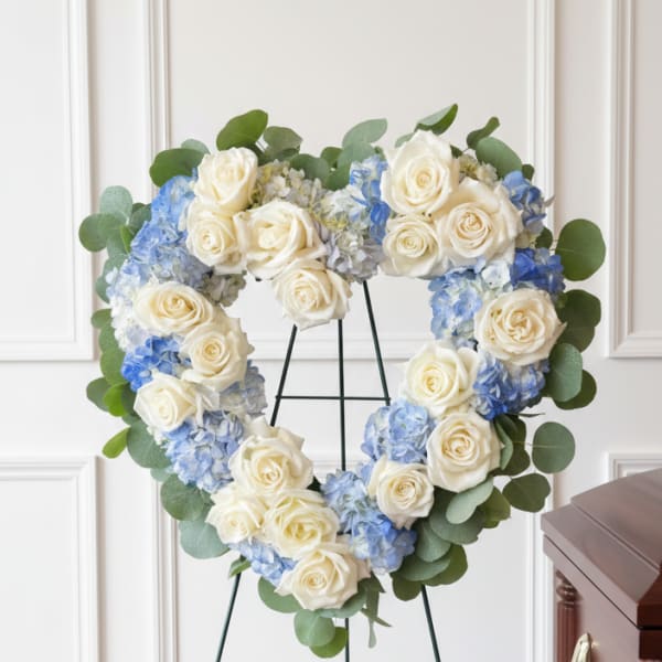 Heart-shaped floral wreath of white roses and blue hydrangeas on a stand