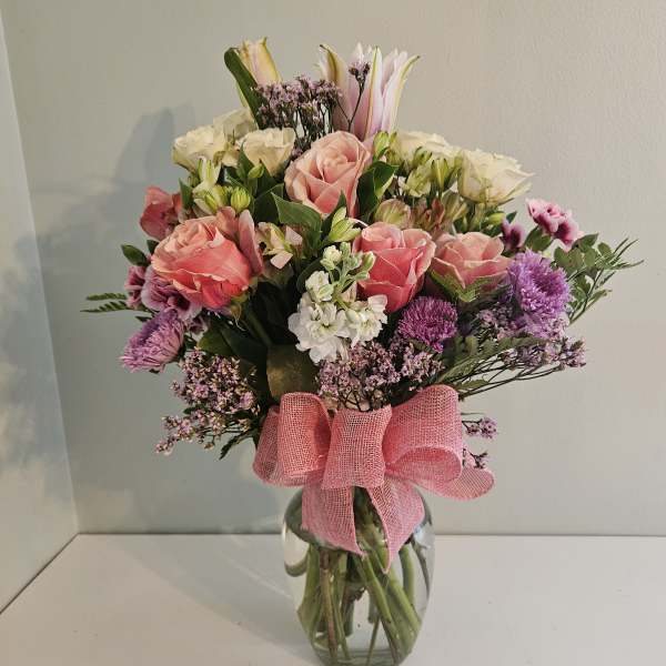 Mixed bouquet of pink and white flowers in a glass vase with a pink ribbon