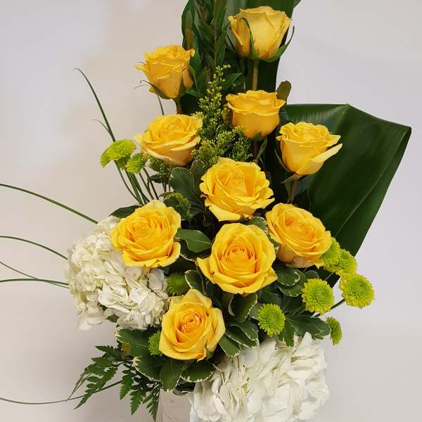 Yellow roses and white hydrangeas in a square vase