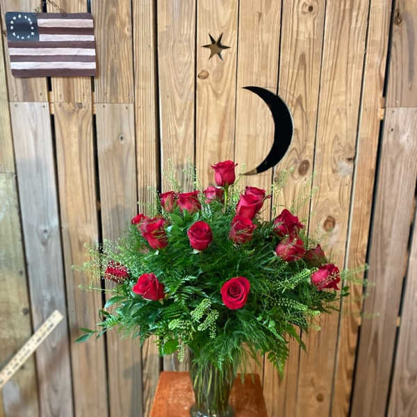 Red roses arranged in a glass vase with greenery