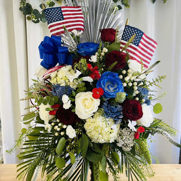Large patriotic floral arrangement with red, white, and blue roses and flags
