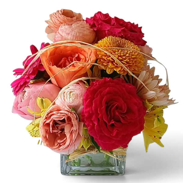 Mixed bouquet of pink, peach, red, and yellow flowers in a square glass vase