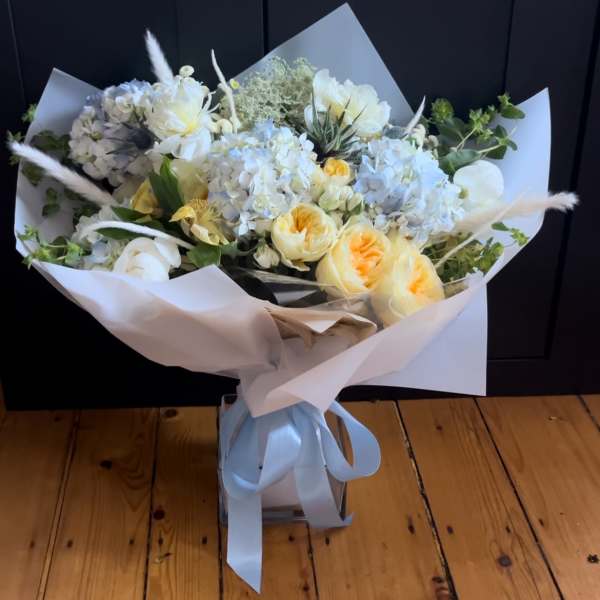Bouquet of white and pale yellow flowers wrapped in white paper with a blue ribbon