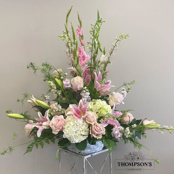 Tall pastel arrangement of pink lilies, roses, and white hydrangeas in a white basket.