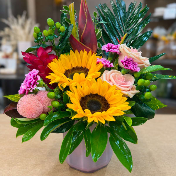 Bright mixed bouquet with sunflowers, roses, and tropical foliage in a vase