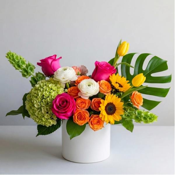 Bright mixed bouquet in a white cylinder vase with roses, tulips, and sunflowers