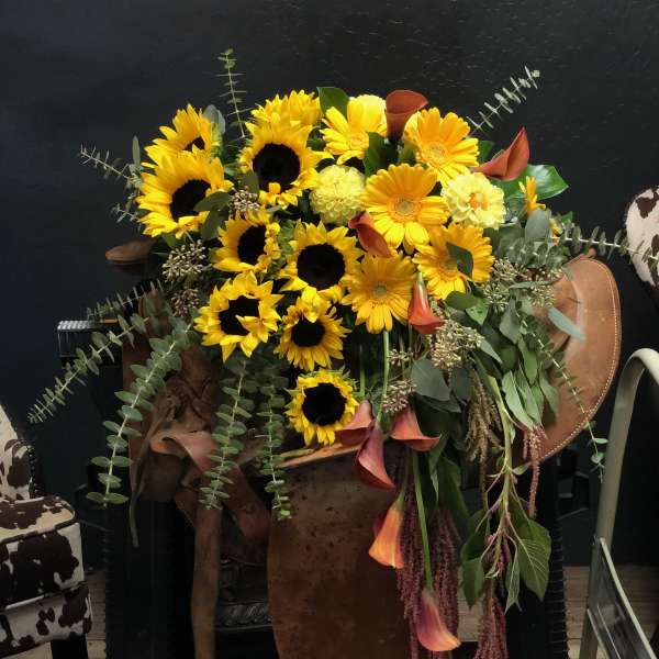 Large bouquet of yellow sunflowers and orange calla lilies in a rustic container