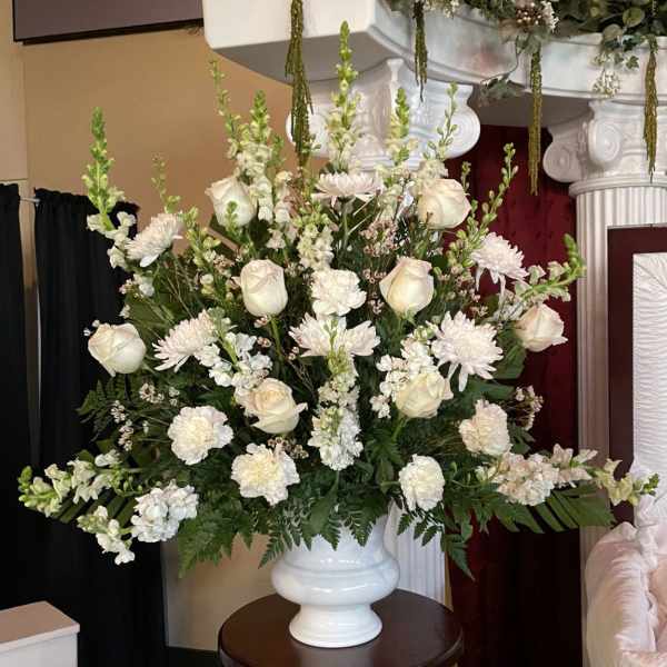 Large white arrangement of roses, carnations, and chrysanthemums in a white urn-style vase