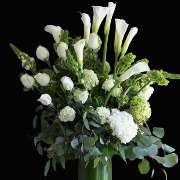 White calla lilies and hydrangeas in a tall glass vase
