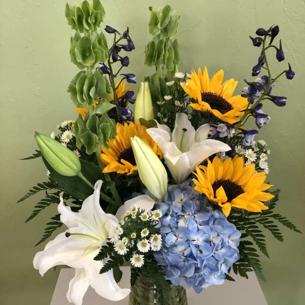 Bouquet of sunflowers, white lilies, blue hydrangea, and purple flowers in a glass vase