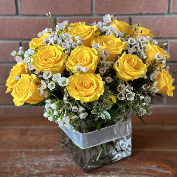Yellow roses arranged in a square glass vase with small white filler flowers