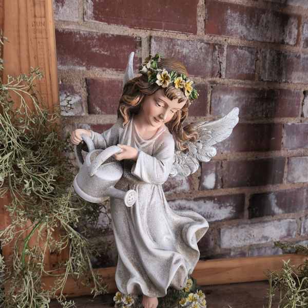 Angel figurine holding a watering can with small flowers on her head and base
