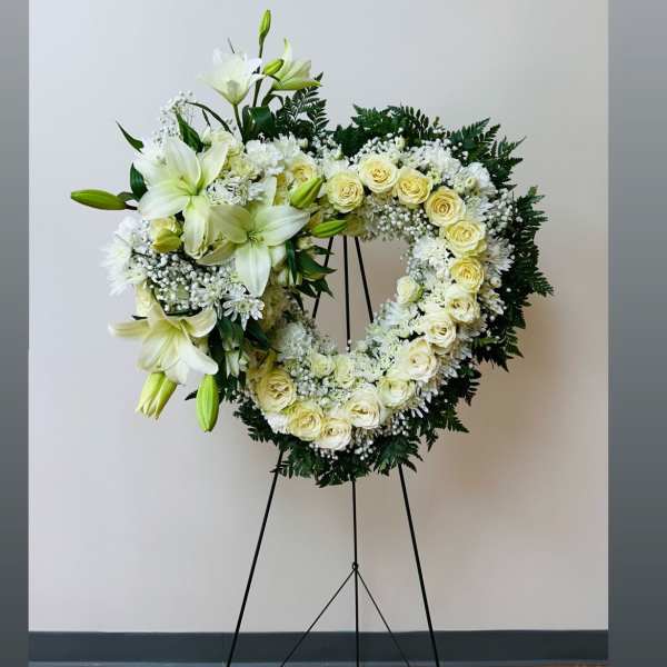 Heart-shaped white floral wreath on a stand with lilies and roses