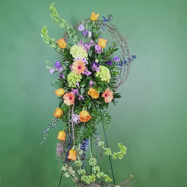 Tall floral arrangement with orange roses, gerbera daisies, and purple blooms