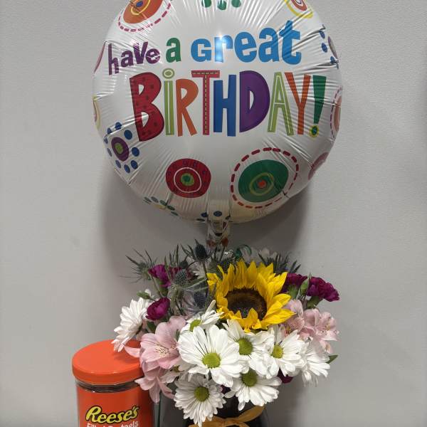 Birthday balloon above a mixed flower arrangement with a candy container