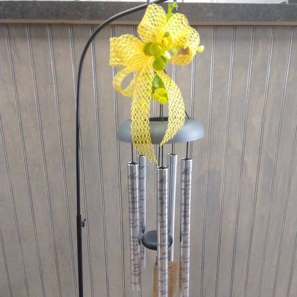 Yellow ribbon-topped wind chime with silver tubes on a black stand