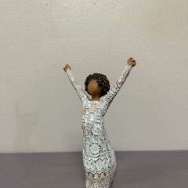Small decorative figurine of a person with raised arms in a patterned dress
